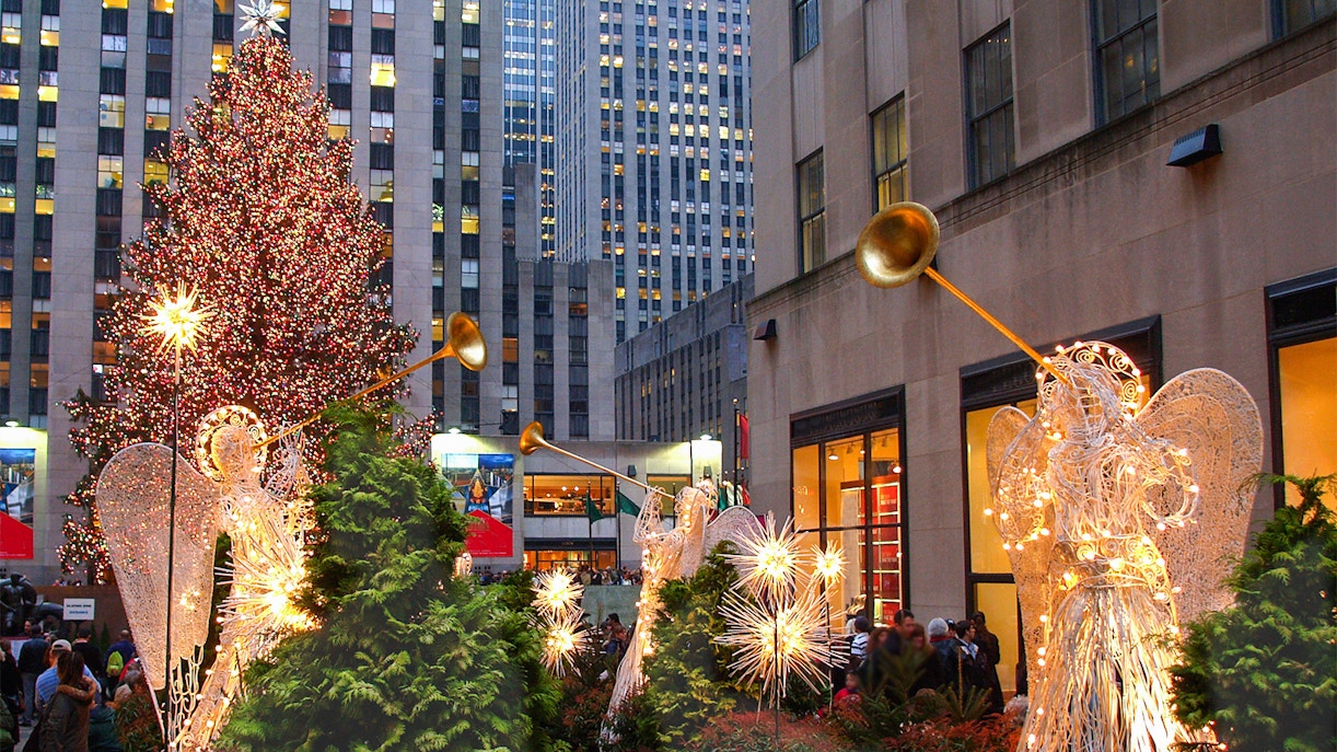 Rockefeller Center Christmas Tree with illuminated angels and city buildings in New York City.
