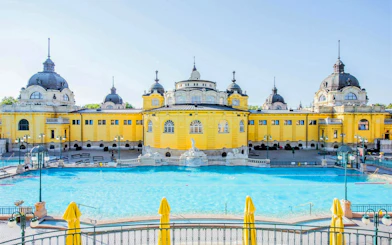 Széchenyi Spa thermal pool with historic yellow building in Budapest.