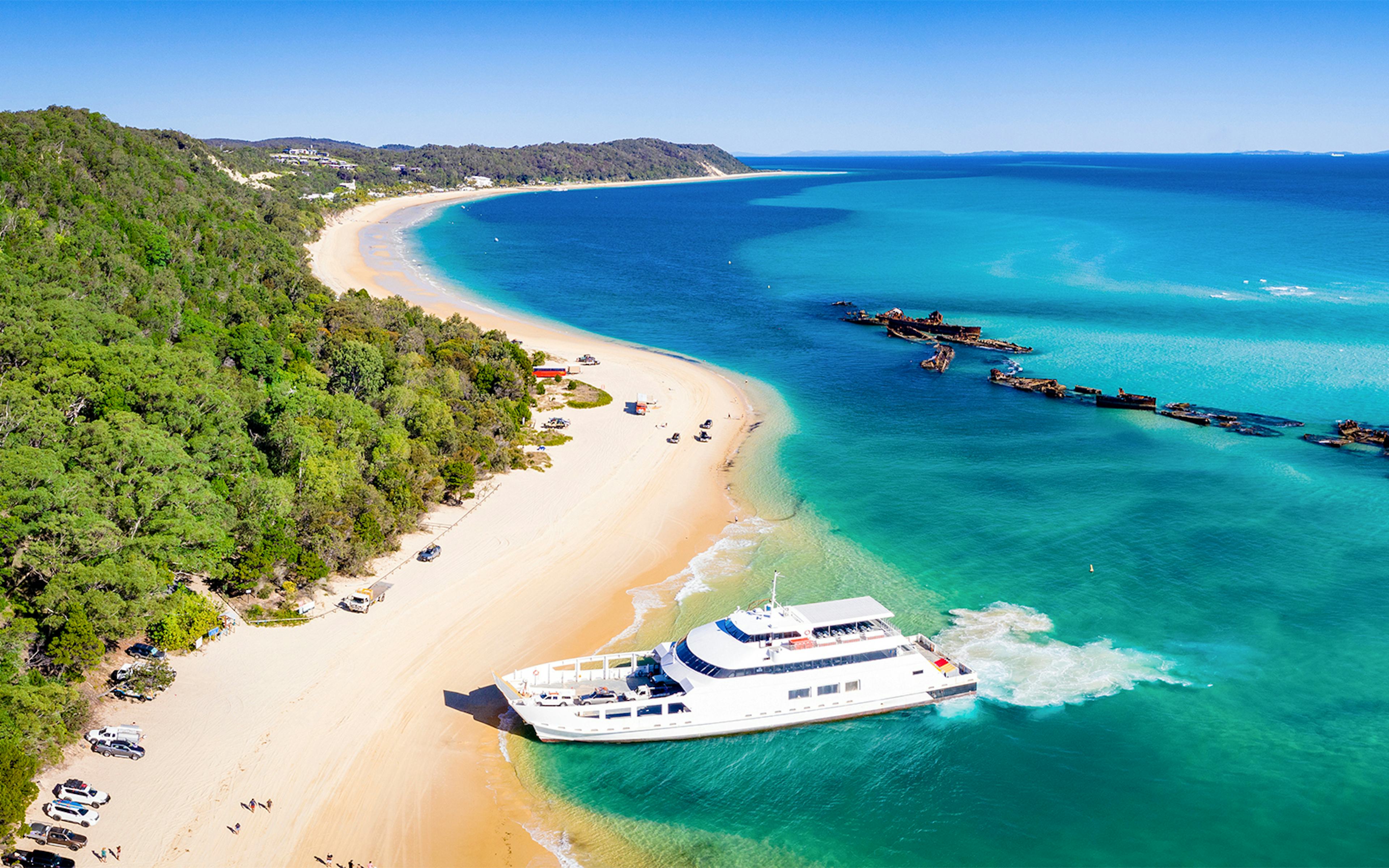 Moreton Island beach with shipwrecks, kayaks, and 4WD vehicles along the shore.