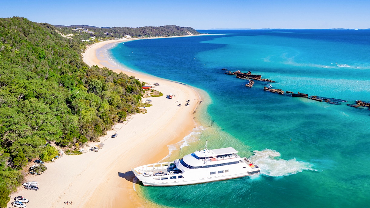 Moreton Island beach with shipwrecks, kayaks, and 4WD vehicles along the shore.