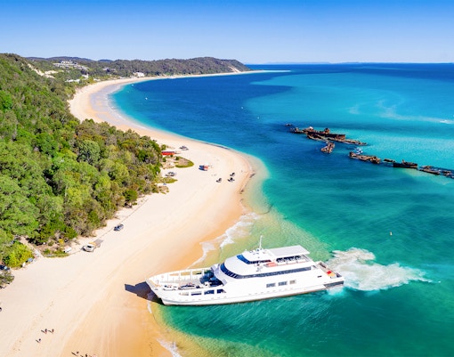 Moreton Island beach with shipwrecks, kayaks, and 4WD vehicles along the shore.