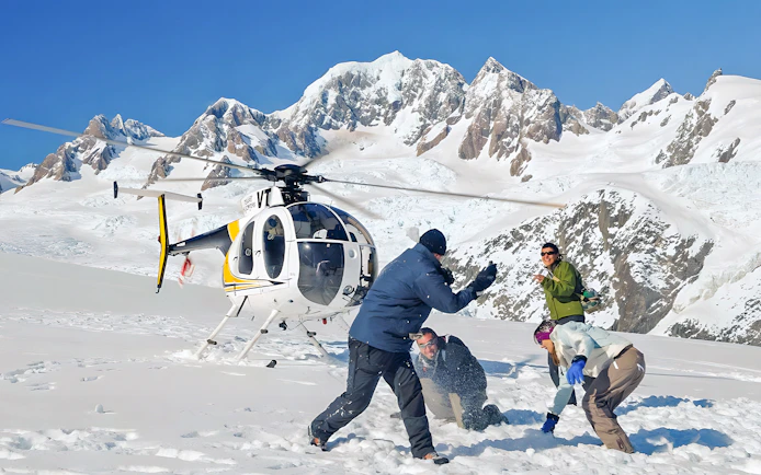 People enjoying snow on Franz Josef Glacier with a helicopter in the background.