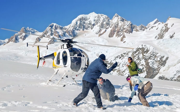 People enjoying snow on Franz Josef Glacier with a helicopter in the background.