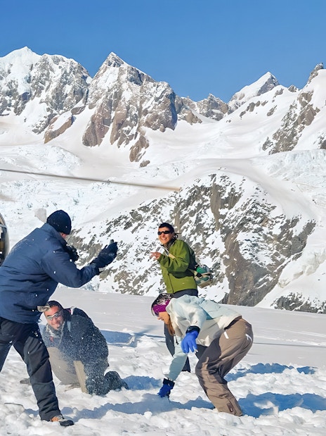 People enjoying snow on Franz Josef Glacier with a helicopter in the background.