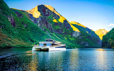 Cruise ship on Nærøyfjord surrounded by steep green mountains, Western Norway.