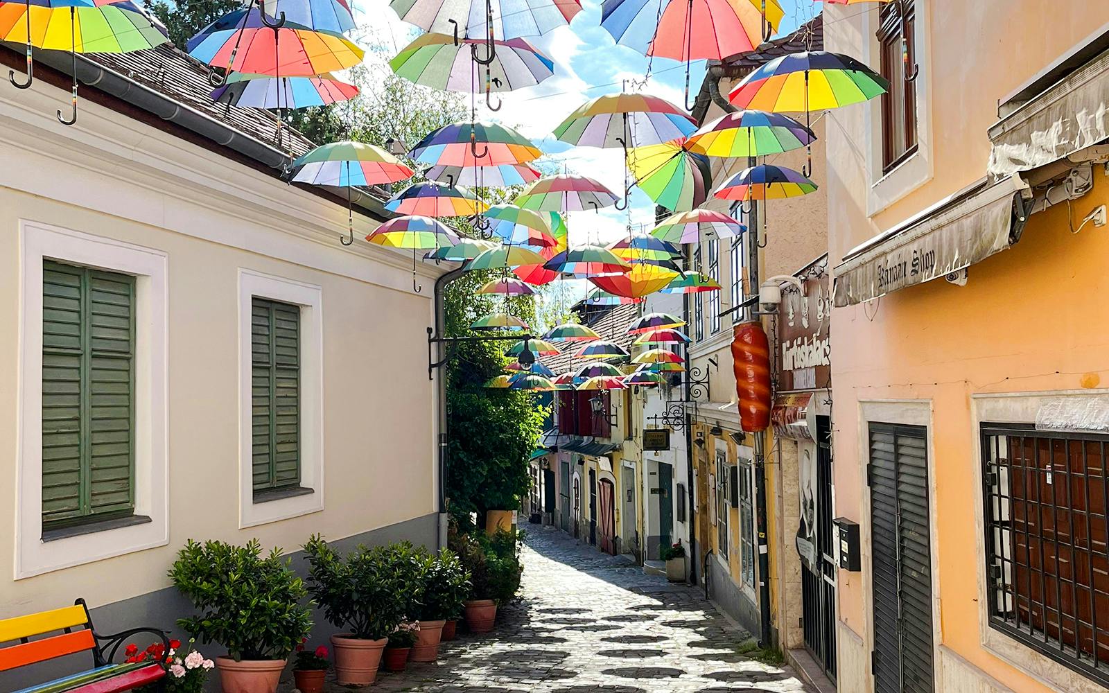 Cobbled street in Szentendre, Hungary, with colorful umbrellas hanging above.