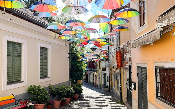 Cobbled street in Szentendre, Hungary, with colorful umbrellas hanging above.