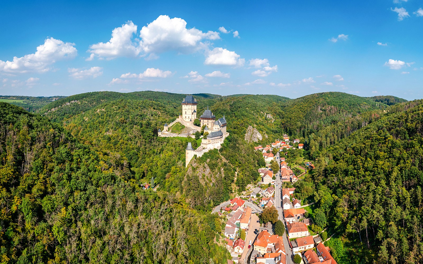 Karlstejn Castle overlooking the village surrounded by lush green hills.