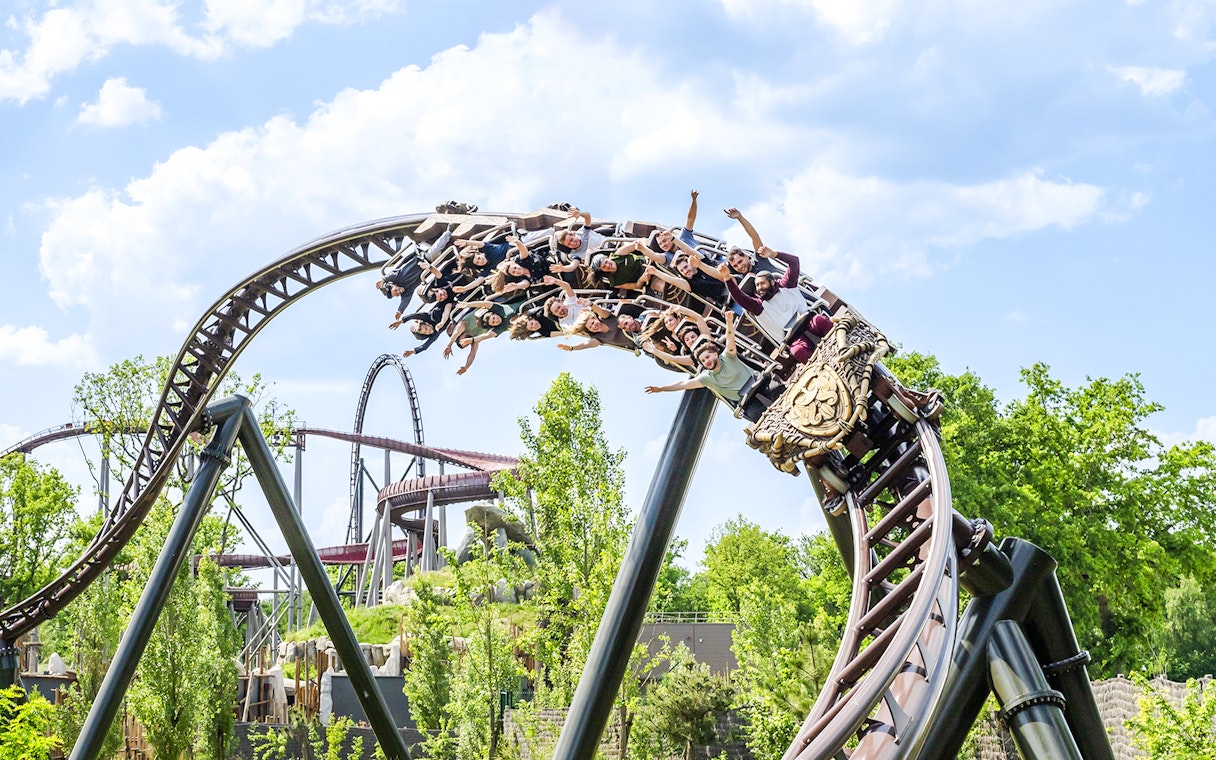 Roller coaster with riders at Parc Asterix, France, surrounded by greenery.