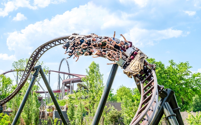 Roller coaster with riders at Parc Asterix, France, surrounded by greenery.