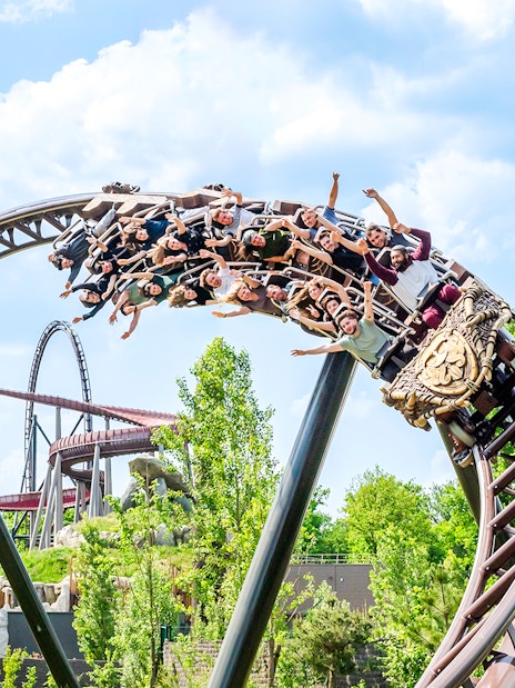 Roller coaster with riders at Parc Asterix, France, surrounded by greenery.