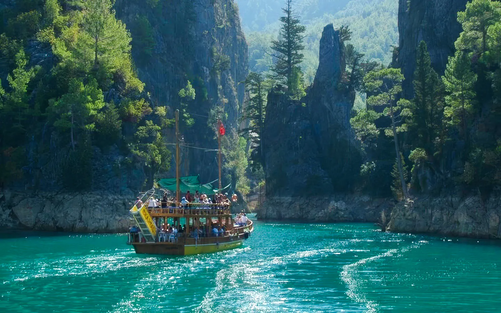Boat navigating through Green Canyon with tourists, surrounded by lush cliffs, during tour from Alanya.