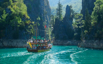 Boat navigating through Green Canyon with tourists, surrounded by lush cliffs, during tour from Alanya.