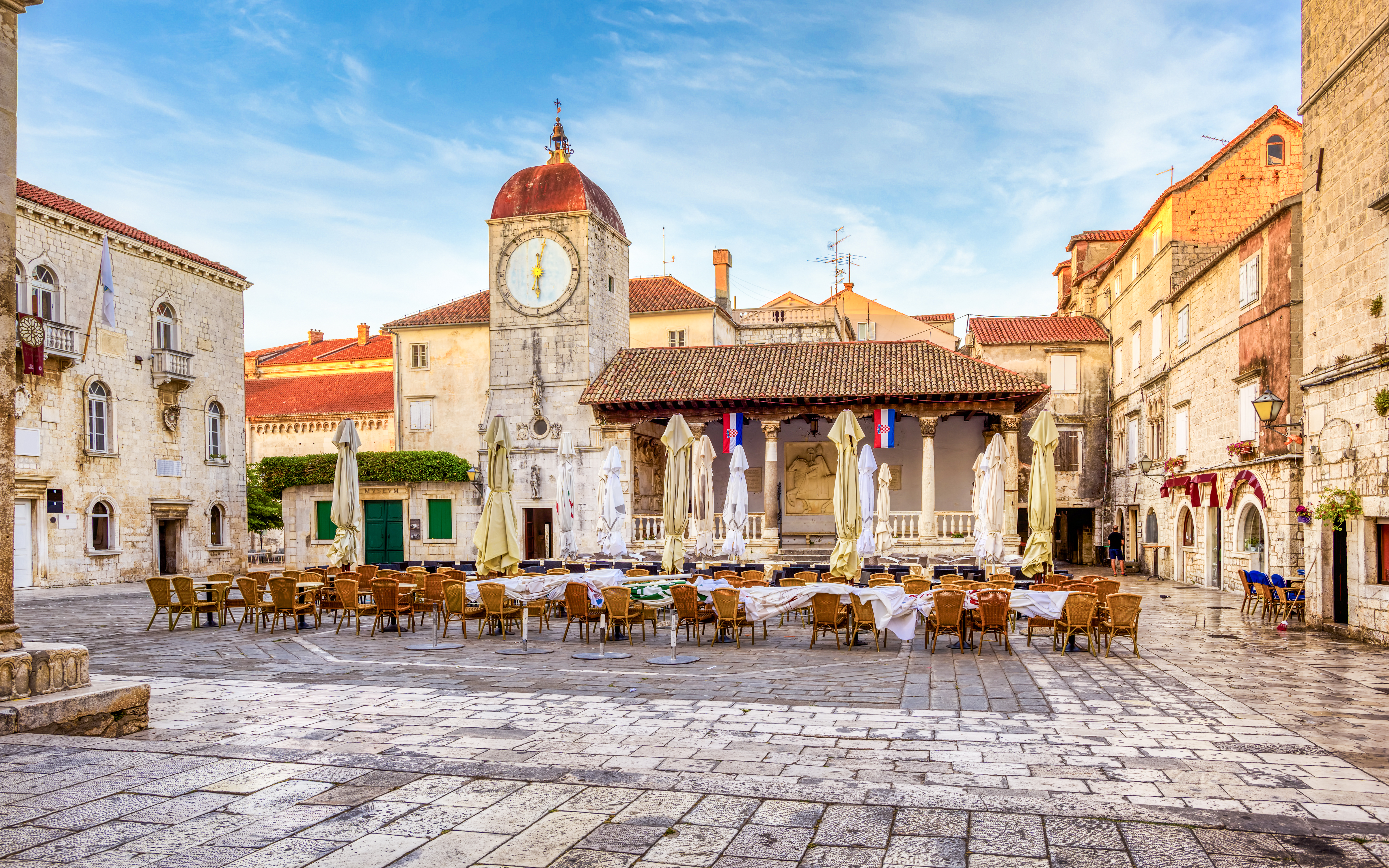Central square in Trogir Old Town, Croatia with clock tower and outdoor seating.