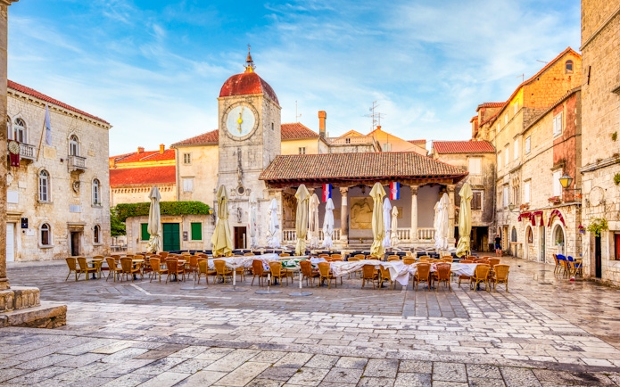 Central square in Trogir Old Town, Croatia with clock tower and outdoor seating.