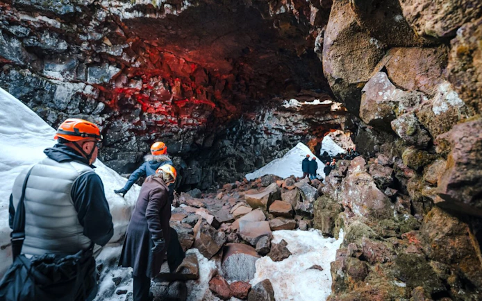 Guests exploring Raufarhólshellir Lava Tunnel with helmets and winter gear.