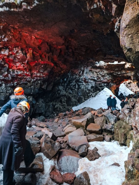 Guests exploring Raufarhólshellir Lava Tunnel with helmets and winter gear.
