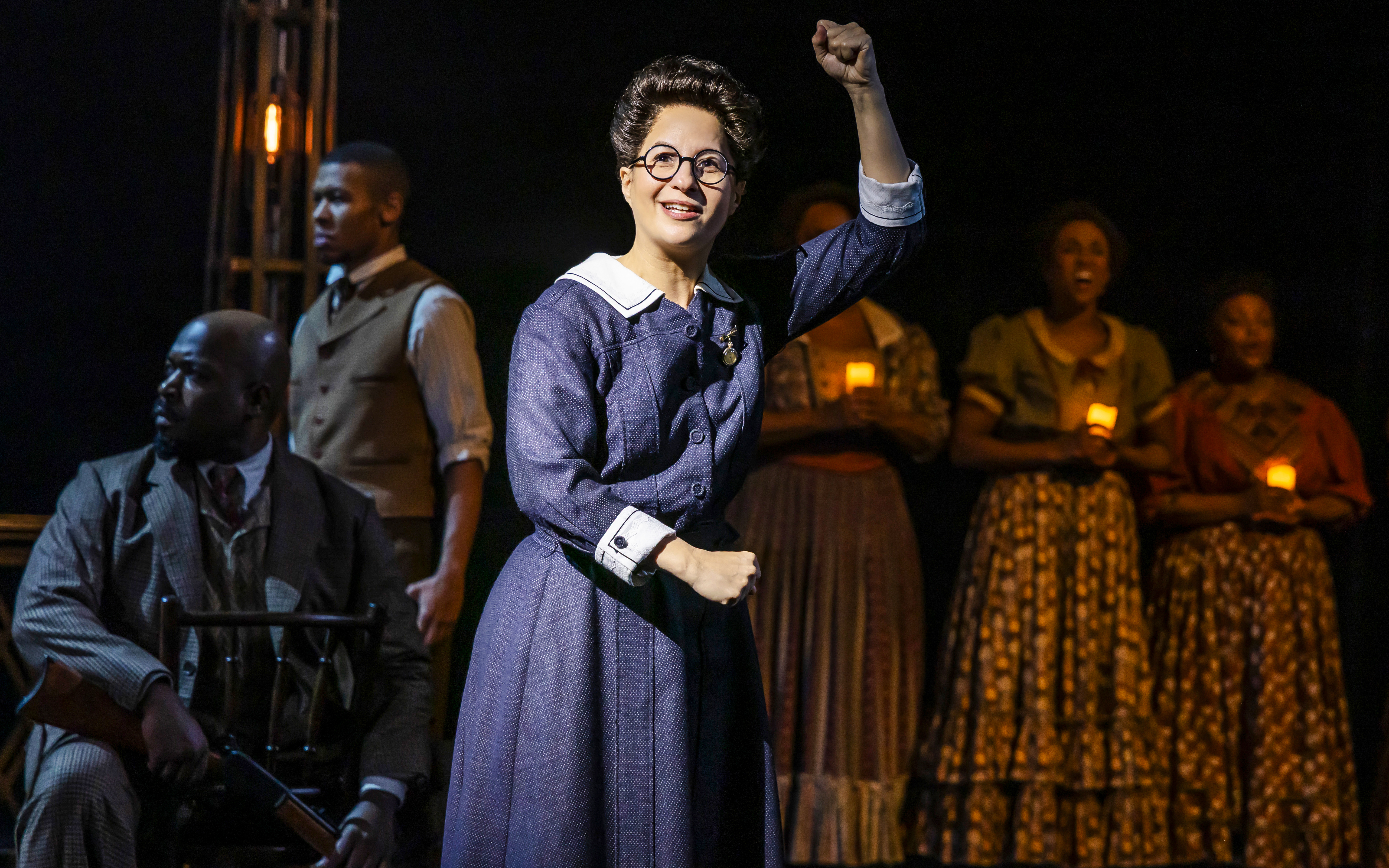 Performer raising fist during Ragtime musical scene with ensemble holding candles.