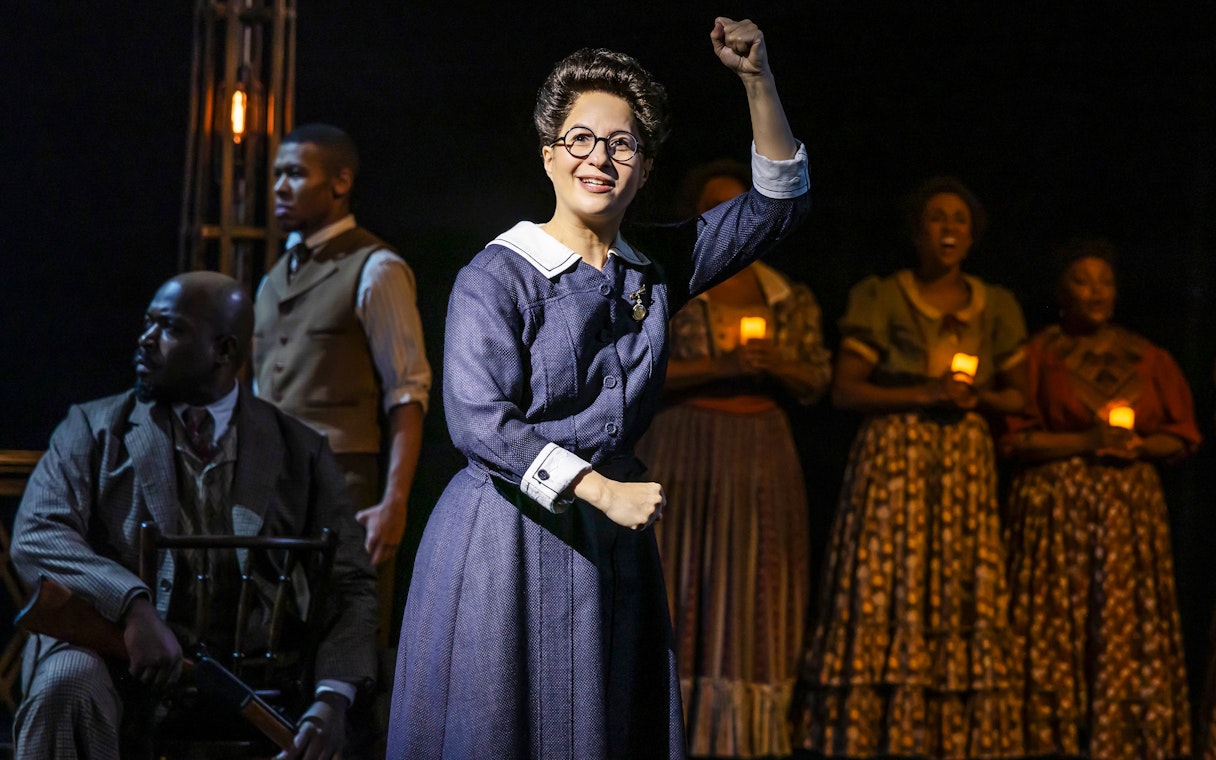Performer raising fist during Ragtime musical scene with ensemble holding candles.