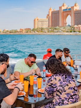 Group dining on a boat with Atlantis The Palm, Dubai in the background.