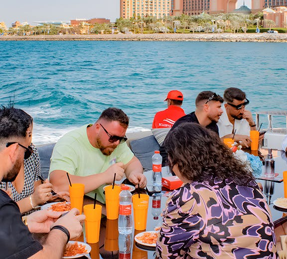Group dining on a boat with Atlantis The Palm, Dubai in the background.