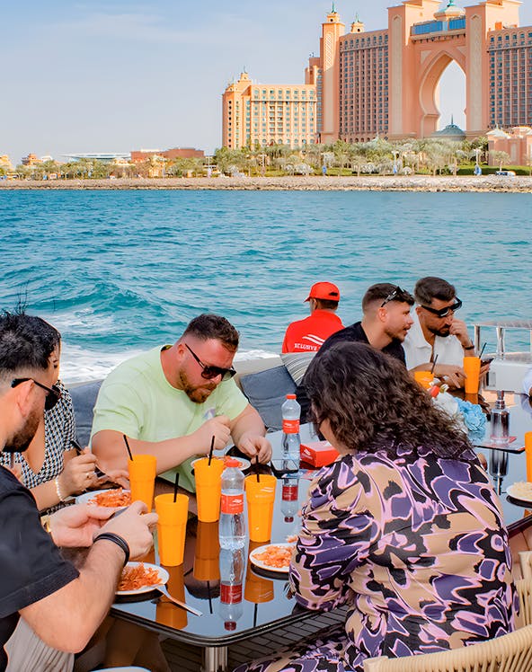Group dining on a boat with Atlantis The Palm, Dubai in the background.