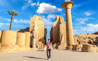 Tourist exploring Luxor Temple with ancient columns and statues, Egypt.