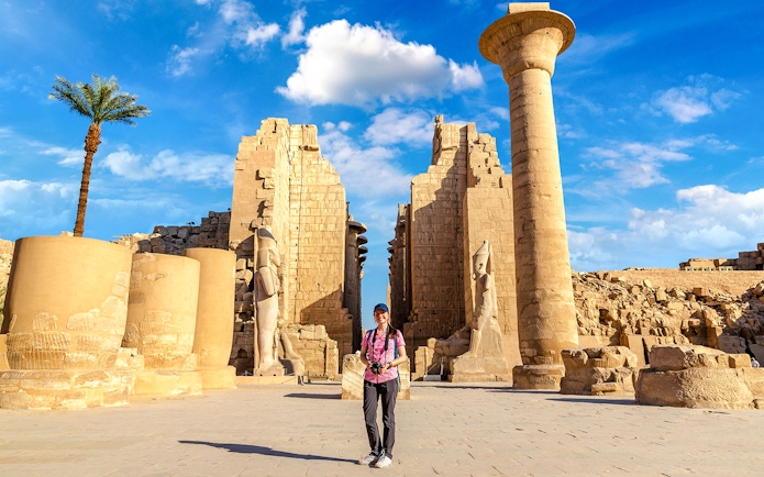 Tourist exploring Luxor Temple with ancient columns and statues, Egypt.