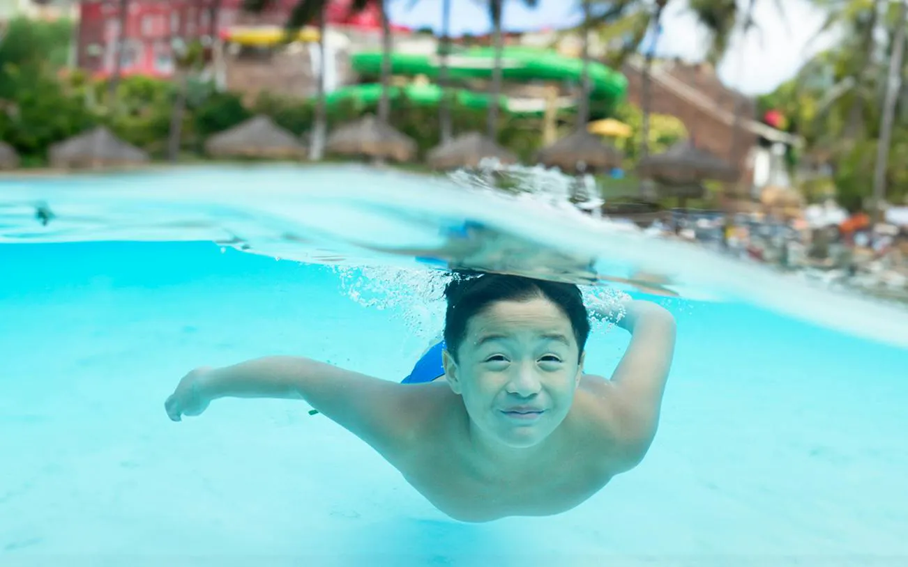 Child swimming underwater at Wet 'n' Wild Hawaii, Oahu, with water slides in the background.