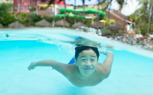 Child swimming underwater at Wet 'n' Wild Hawaii, Oahu, with water slides in the background.