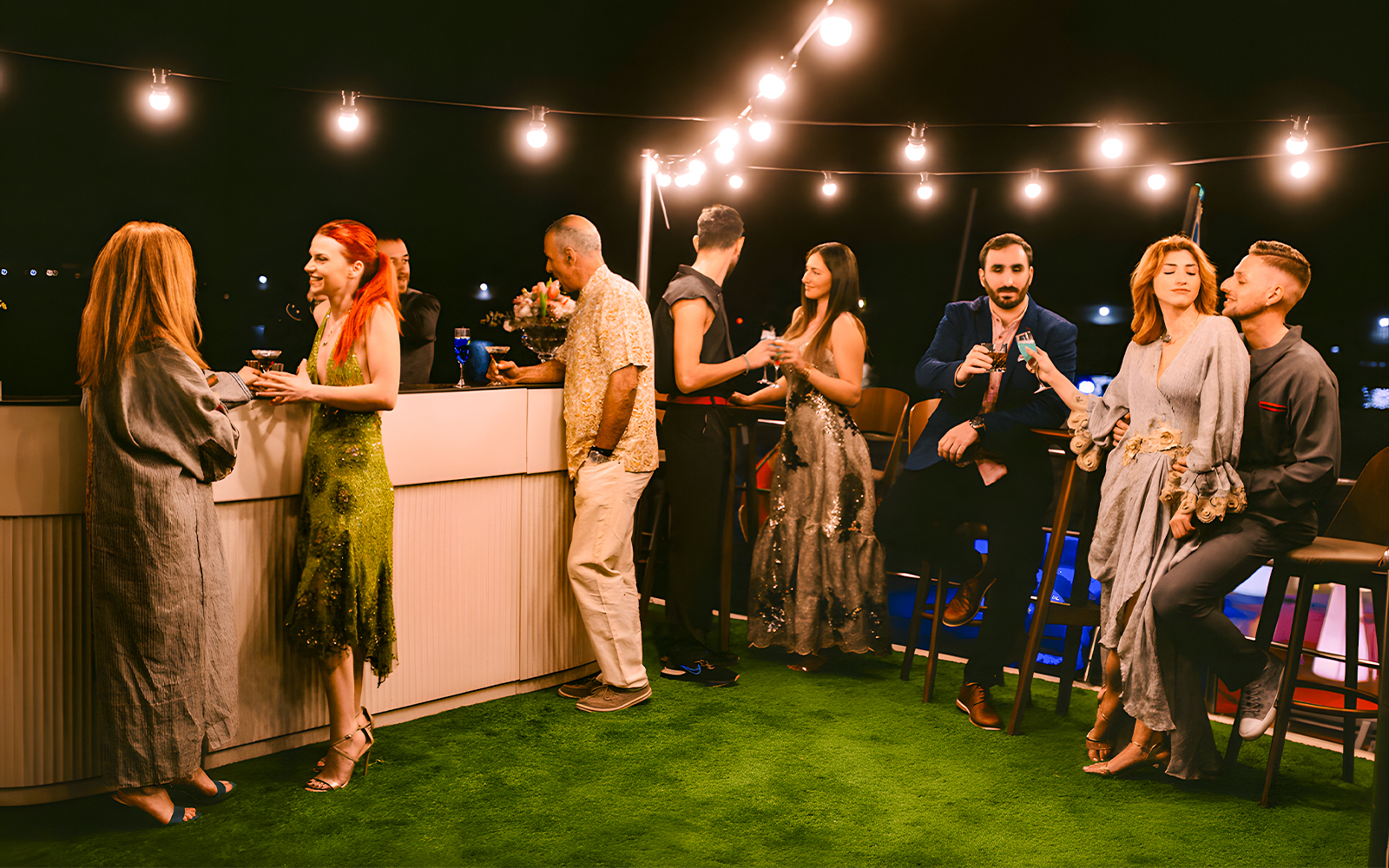 Guests socializing on Athens Riviera evening cruise with city lights in background.