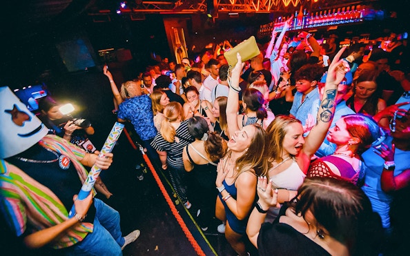Partygoers dancing at a lively Prague boat party with vibrant lights.