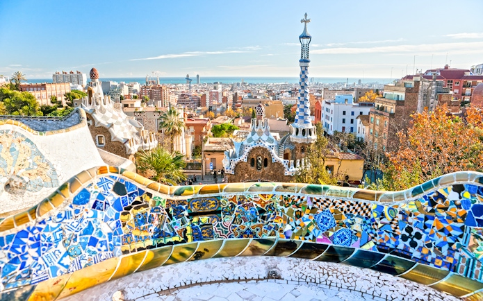 Panoramic view of Park Güell's colorful mosaic terrace overlooking Barcelona.
