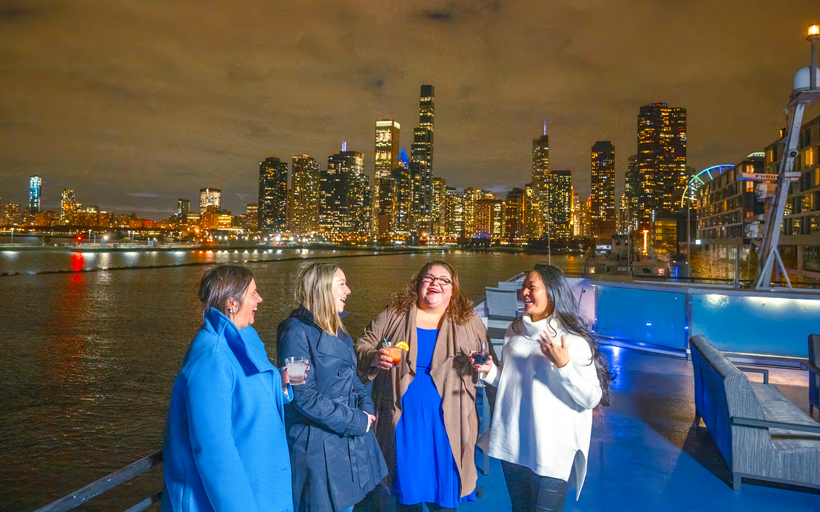 Group enjoying drinks on a Chicago dinner cruise with city skyline at night.
