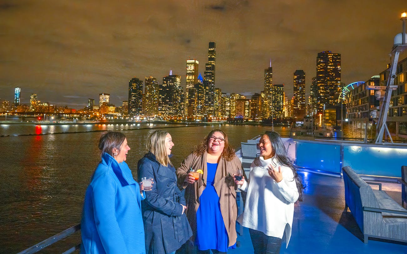 Group enjoying drinks on a Chicago dinner cruise with city skyline at night.