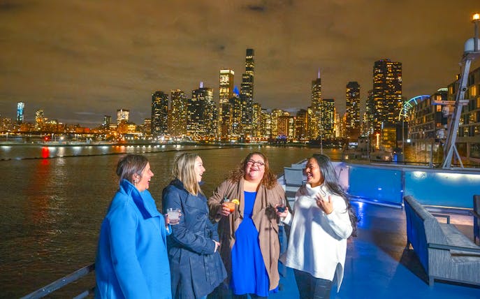 Group enjoying drinks on a Chicago dinner cruise with city skyline at night.