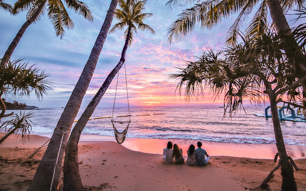 Couples sitting on Hon Thom beach at sunset, Phu Quoc, with palm trees and ocean view.