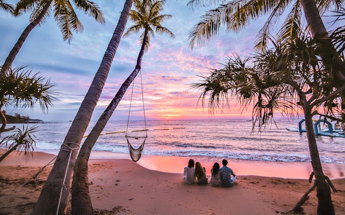 Couples sitting on Hon Thom beach at sunset, Phu Quoc, with palm trees and ocean view.
