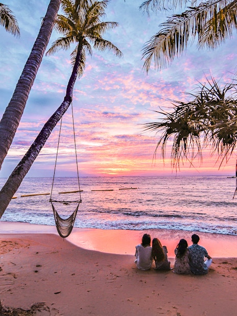 Couples sitting on Hon Thom beach at sunset, Phu Quoc, with palm trees and ocean view.