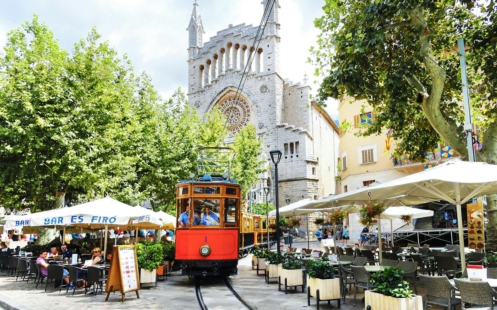Vintage train passing by a café and church in Sóller, Mallorca.