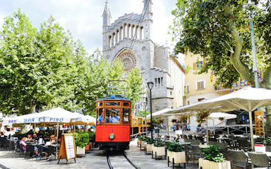 Vintage train passing by a café and church in Sóller, Mallorca.