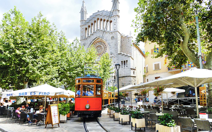 Vintage train passing by a café and church in Sóller, Mallorca.