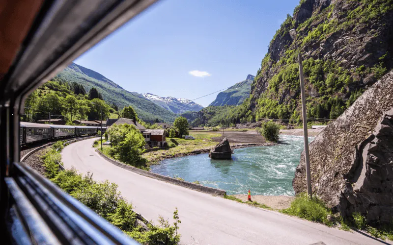 Bergen to Flåm train view of river, mountains, and houses on Nærøyfjord UNESCO tour.