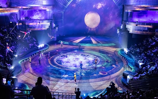 Acrobats performing on La Perle By Dragone theatre stage with vibrant lighting and audience.