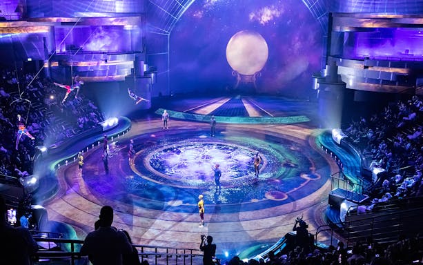Acrobats performing on La Perle By Dragone theatre stage with vibrant lighting and audience.