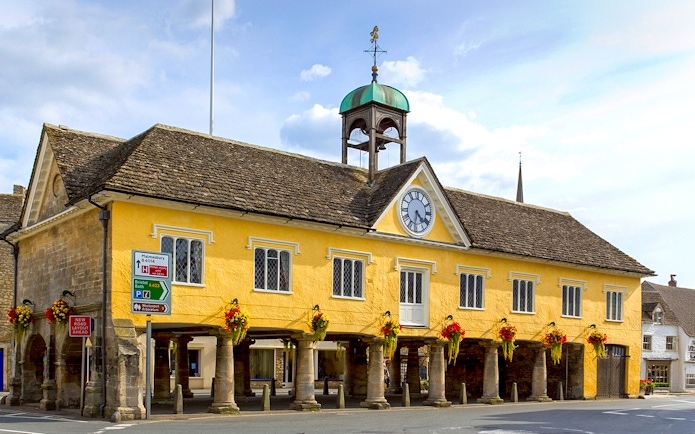 Historic market hall in Cotswolds with clock tower and floral decorations.