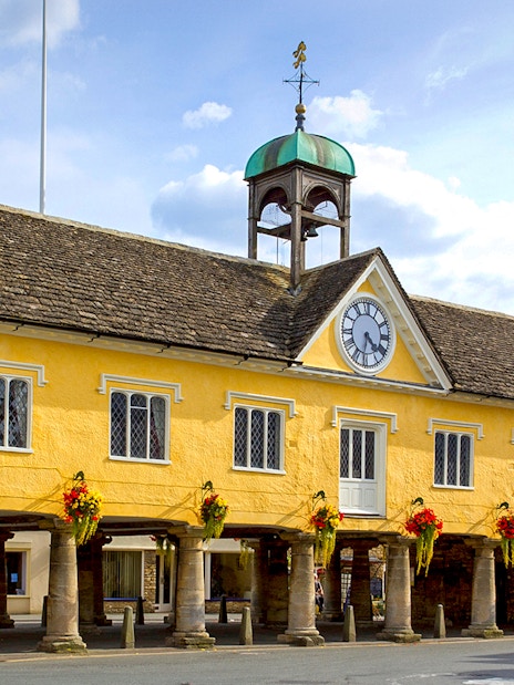 Historic market hall in Cotswolds with clock tower and floral decorations.