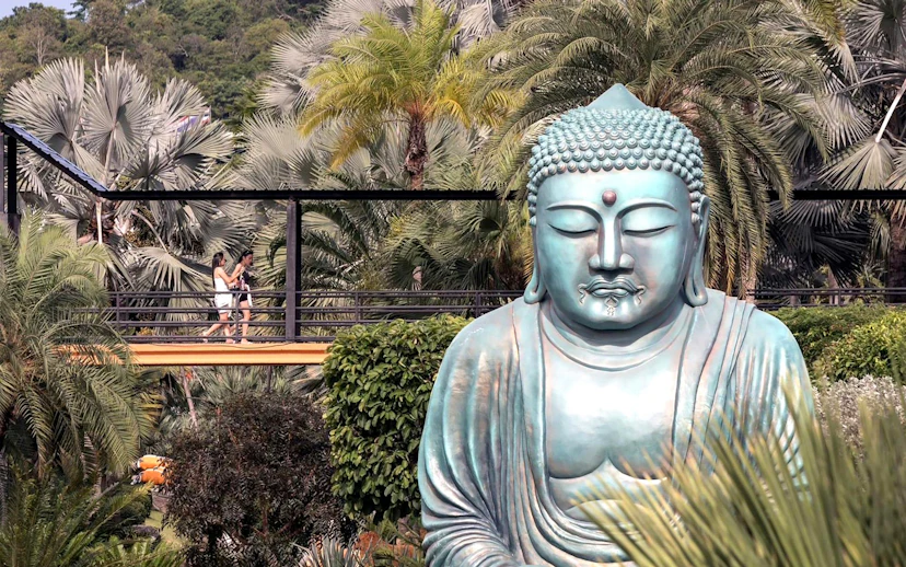 Buddha statue surrounded by tropical plants at Nong Nooch Tropical Garden, Thailand.