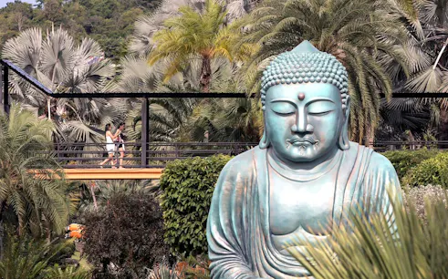 Buddha statue surrounded by tropical plants at Nong Nooch Tropical Garden, Thailand.