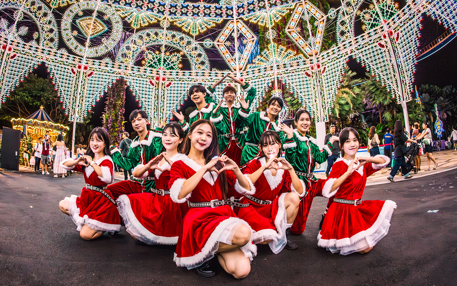 Performers in festive costumes at Gardens by the Bay, Singapore, with illuminated decorations.